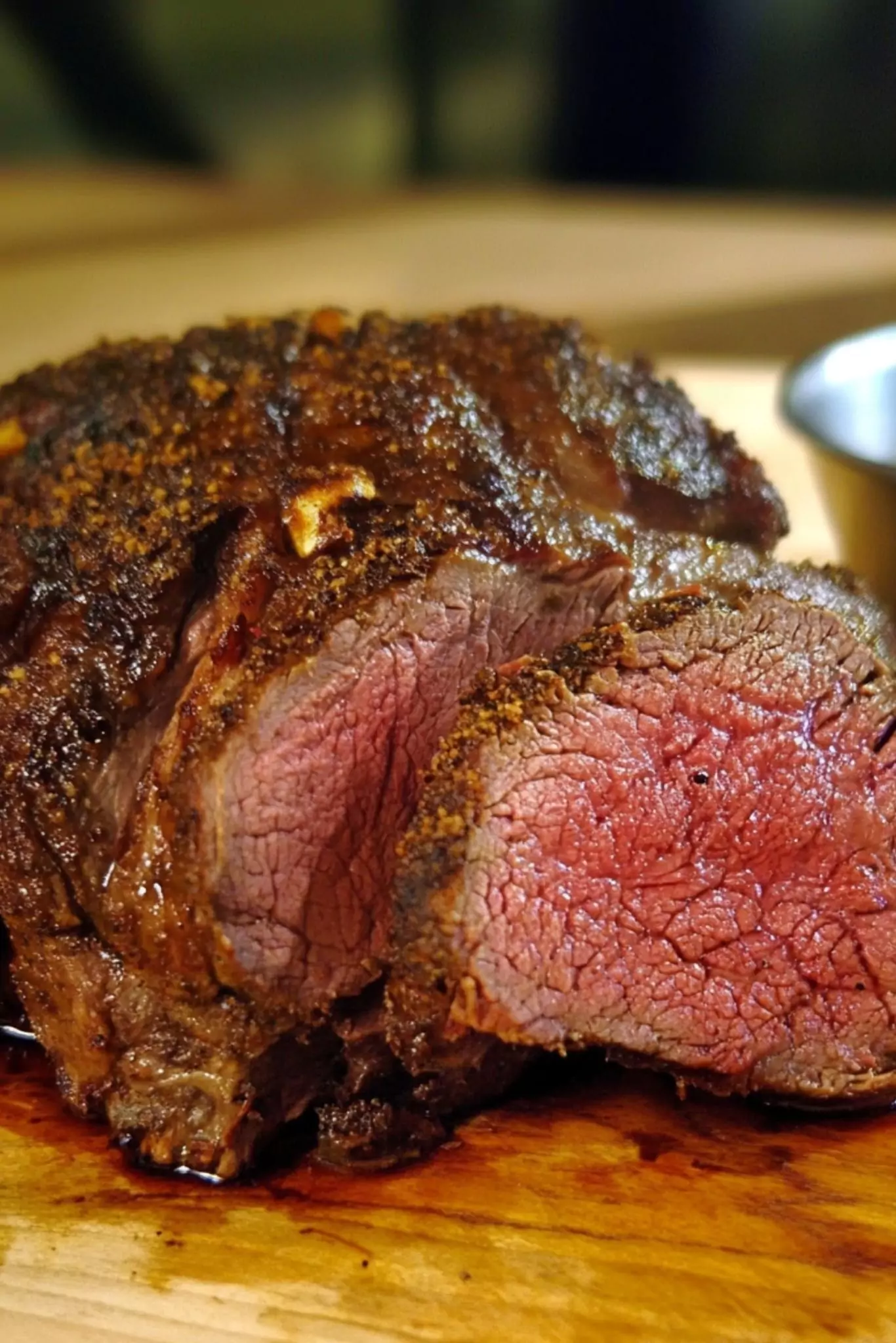 Sliced venison roast showing a medium-rare center and seasoned crust, served on a wooden cutting board.