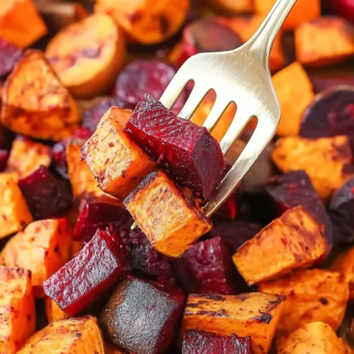 Fork holding roasted beets and roasted sweet potatoes over a tray of oven-baked root vegetables.